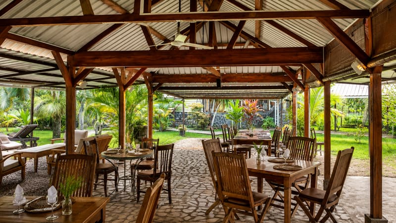 La salle sous varangue, tables en bois dressées, ouverte sur le jardin